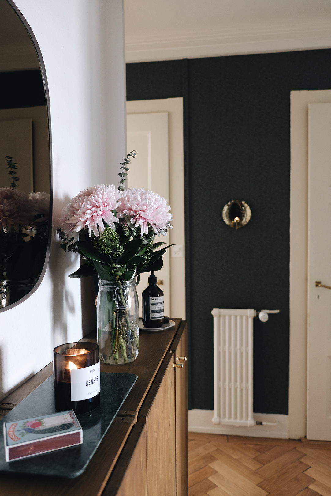 Entryway with brass candle sconce on dark green wallpaper